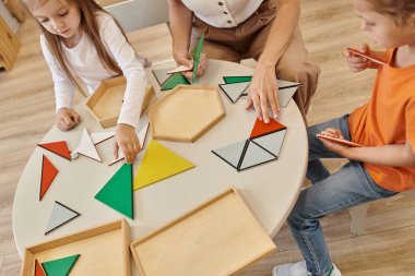 high angle view of teacher and kids playing with triangles on table in montessori school clipart