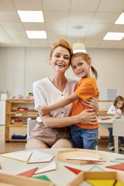 Pozitif öğrenci kucaklama öğretmeni ve Montessori okulunda kameraya bakıyor.