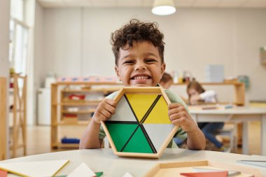 Bulanık montessori okulunda ahşap didactic malzemeler tutan Afro-Amerikan çocuk