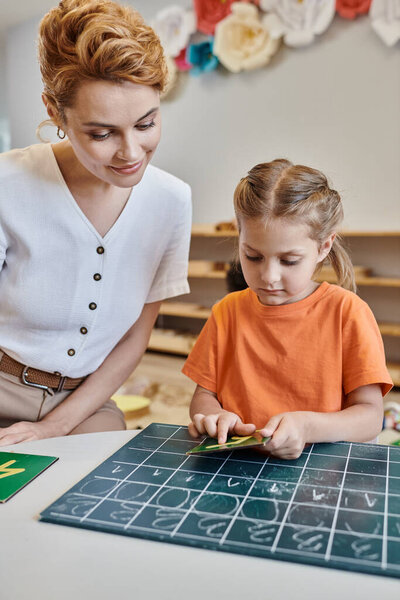 умная девочка, указывающая на число рядом с учителем, считая на доске, учась через игру, Монтессори