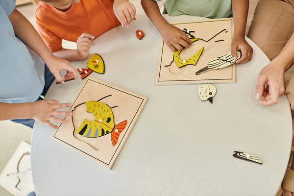 top view, cropped interracial kids playing with didactic montessori material in school, puzzle