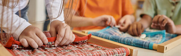partial view of child playing with cloth and buttons in montessori school, banner