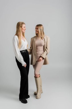Resmi giyinmiş, gülümseyen ve birbirine bakan iki güzel sarışın kız kardeş, moda konsepti.