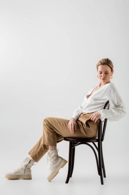 Şık giyinmiş şık sarışın kadın sandalyede oturuyor ve rahatlıyor, stil ve moda.