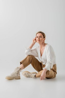 İş hayatında çekici sarışın kadın. Günlük pastel kıyafetler. Yerde oturuyor, stil ve moda.
