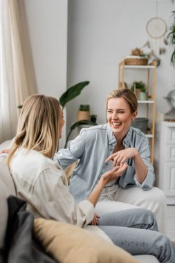 Çekici, sevimli kız kardeşler gündelik giysiler içinde kanepede oturuyor ve içtenlikle gülümsüyor, aile bağı kuruyor.