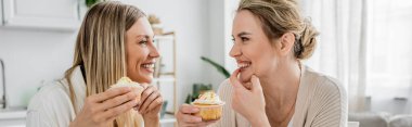 Pastel kıyafetli çekici kızlar mutfak zemininde keklerin tadını çıkarıyorlar, bağlanıyorlar, afiş yapıyorlar.