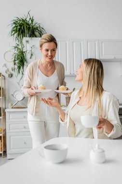Pastel elbiseli, konuşan ve gülümseyen iki kız kardeş, ellerinde kekler, aile bağları.