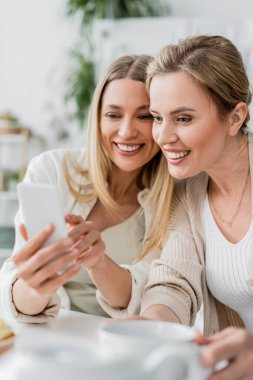 İyi görünümlü iki kız kardeşi cep telefonlarına bakıp gülümsüyorlar, aile bağı kuruyorlar.