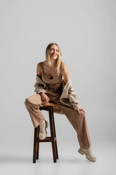 Stock image cheerful blonde woman in stylish formal suit sitting on chair and smiling, fashion and style