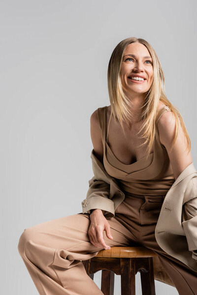 close up of happy smiling blonde woman in beige formal suit sitting on chair, fashion concept