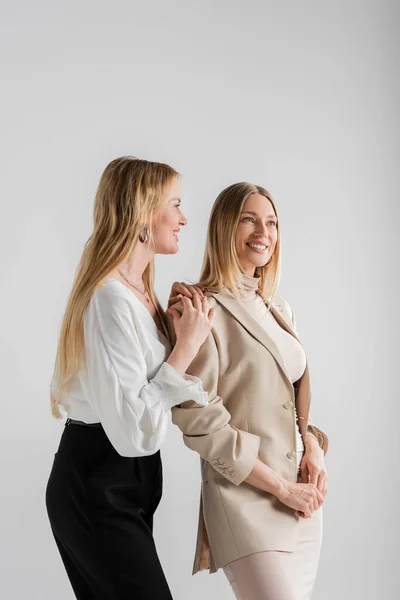 stock image two cheerful attractive blonde sisters smiling and posing on grey backdrop, fashion concept