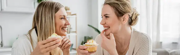 stock image attractive classy sisters in pastel outfit enjoying cupcakes on kitchen backdrop, bonding, banner