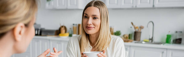cropped view of two pretty lovely sisters talking and drinking tea, family bonding, banner