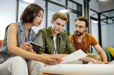 young architect looking at document near blueprint and businessmen in office, startup planning clipart