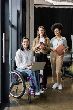Üç ırklar arası iş kadını, tekerlekli sandalyedeki mutlu engelli kadın, kadın takımıyla çalışıyor.