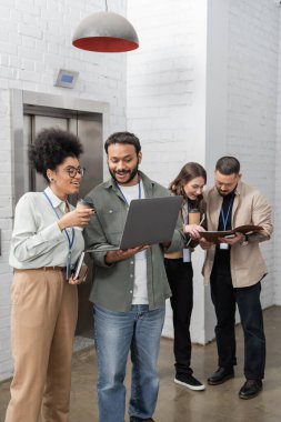 cultural diversity, happy multiethnic colleagues with badges chatting near office elevators, laptop clipart