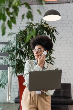 Afro-Amerikan takımı dizüstü bilgisayar kullanarak ve akıllı telefonla konuşarak gözlük takıyor.