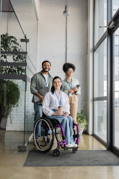 group shot of diverse and inclusive business people looking at camera, wheelchair user in office