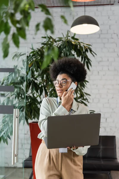 stock image african american team lead in glasses using laptop and talking on smartphone, multitasking