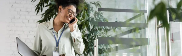 快乐的非洲裔美国女商人 戴着眼镜 拿着笔记本电脑 拿着智能手机和横幅说话 — 图库照片