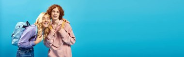 Okul çantalı mutlu ve şık genç sınıf arkadaşları mavi pankartta kameraya bakıyor.