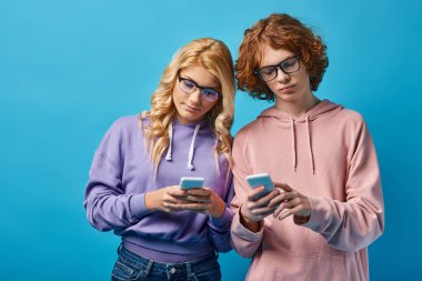 Gözlüklü genç arkadaşlar ve moda kapüşonlular mavi, Z jenerasyonunda akıllı telefonlara bağlanıyorlar.