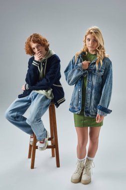 Kızıl saçlı ve şık genç adam, gri, genç modasında sarışın kız arkadaşının yanında yüksek taburede oturuyor.