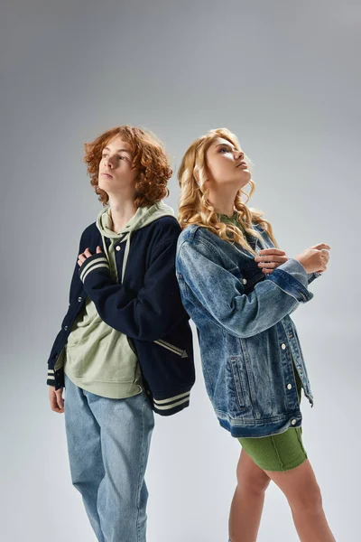 stock image dreamy teenagers in trendy casual attire standing back to back and looking away on grey