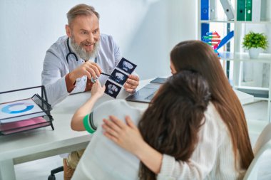 Gri sakallı doktorun yanında sarılıp ultrason gösteren güzel lezbiyen çift.