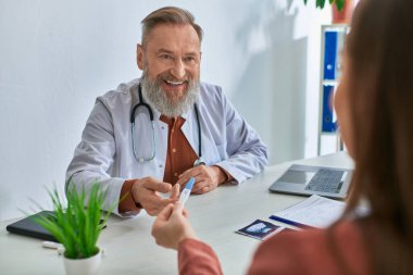 Neşeli doktor, esmer hastasına içtenlikle gülümsüyor hamilelik testi ve konsept gösteriyor.