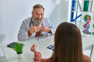 Neşeli gri sakallı doktor hastasına mutlu bir şekilde bakıyor hamilelik testi ve konsept gösteriyor.