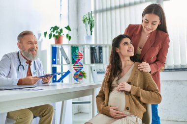 cheerful grey bearded doctor looking happily at loving lesbian couple with hands on pregnant belly clipart