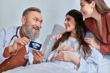 smiley grey bearded doctor showing ultrasound to hugging lgbt couple looking at them, ivf concept clipart