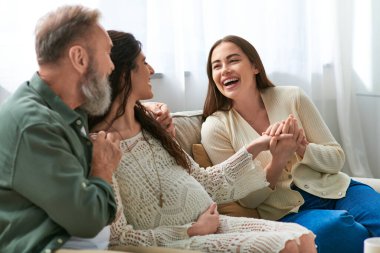 Genç hamile kadın neşeli ortağının elini tutuyor ve babasına gülümsüyor.
