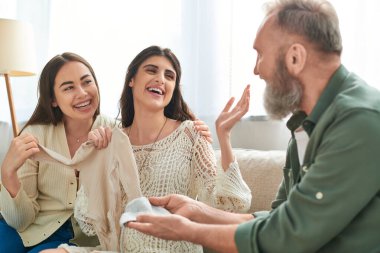 Baba, hamile kızına ve onun neşeli partneri IVF konseptine şapka ve atlet gösteriyor.