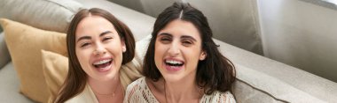 Güzel bir lgbt çifti kanepede oturuyor ve kameraya samimi bir şekilde gülümsüyor.