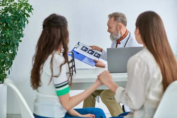 stock image gynecologist showing ultrasound to lgbt couple holding hands and listening to him, ivf concept