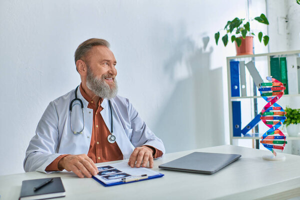 cheerful grey bearded gynecologist with ultrasound on his table smiling in office and looking away