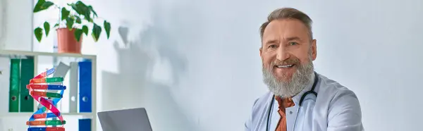 stock image cheerful grey bearded doctor sitting in his office smiling cheerfully and looking at camera