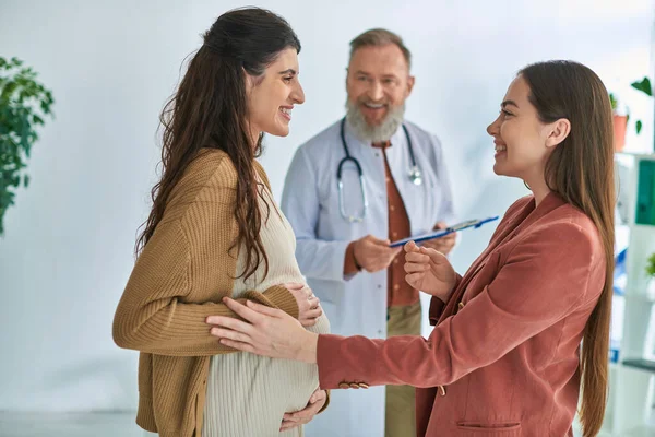 stock image cheerful gynecologist looking at pregnant woman with her partner, in vitro fertilizing concept