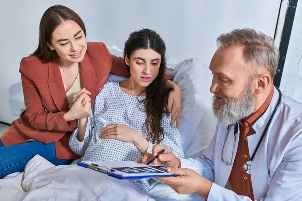 stock image cheerful grey bearded doctor showing ultrasound to lesbian couple, in vitro fertilization concept