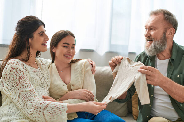 father showing singlet to his daughter and her partner and smiling cheerfully, ivf concept