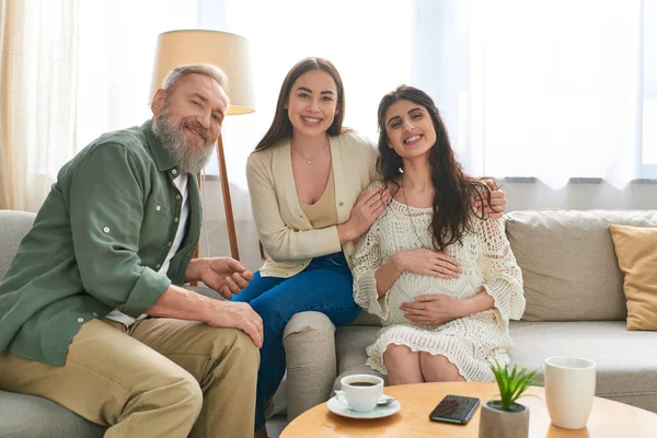 stock image joyous father paying visit to his pregnant daughter and her partner, looking at camera, ivf concept