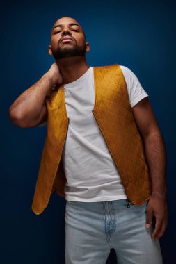Sarı yelekli yakışıklı Afro-Amerikan adam elini boynunun arkasına koyup poz veriyor, moda anlayışı.