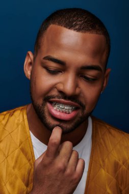 smiley african american male model with braces looking down with finger on chin, fashion concept clipart
