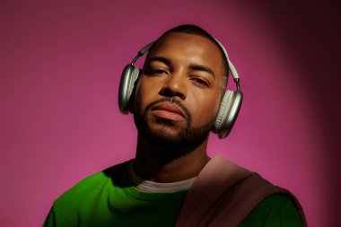 good looking african american man in sweatshirt with headphones on pink backdrop, fashion concept clipart