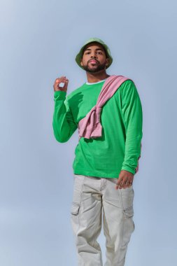 Afro-Amerikan adam elini kaldırmış açık mavi arka planda kameraya bakıyor, moda konsepti.