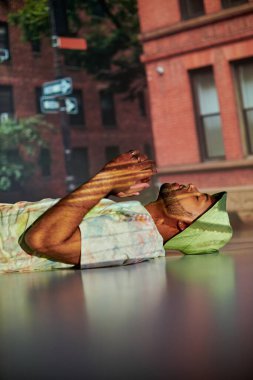 stylish african american man in street wear lying on floor in projector lights, fashion concept clipart