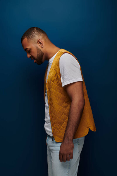 good looking man with beard in yellow vest standing in profile and looking down, fashion concept